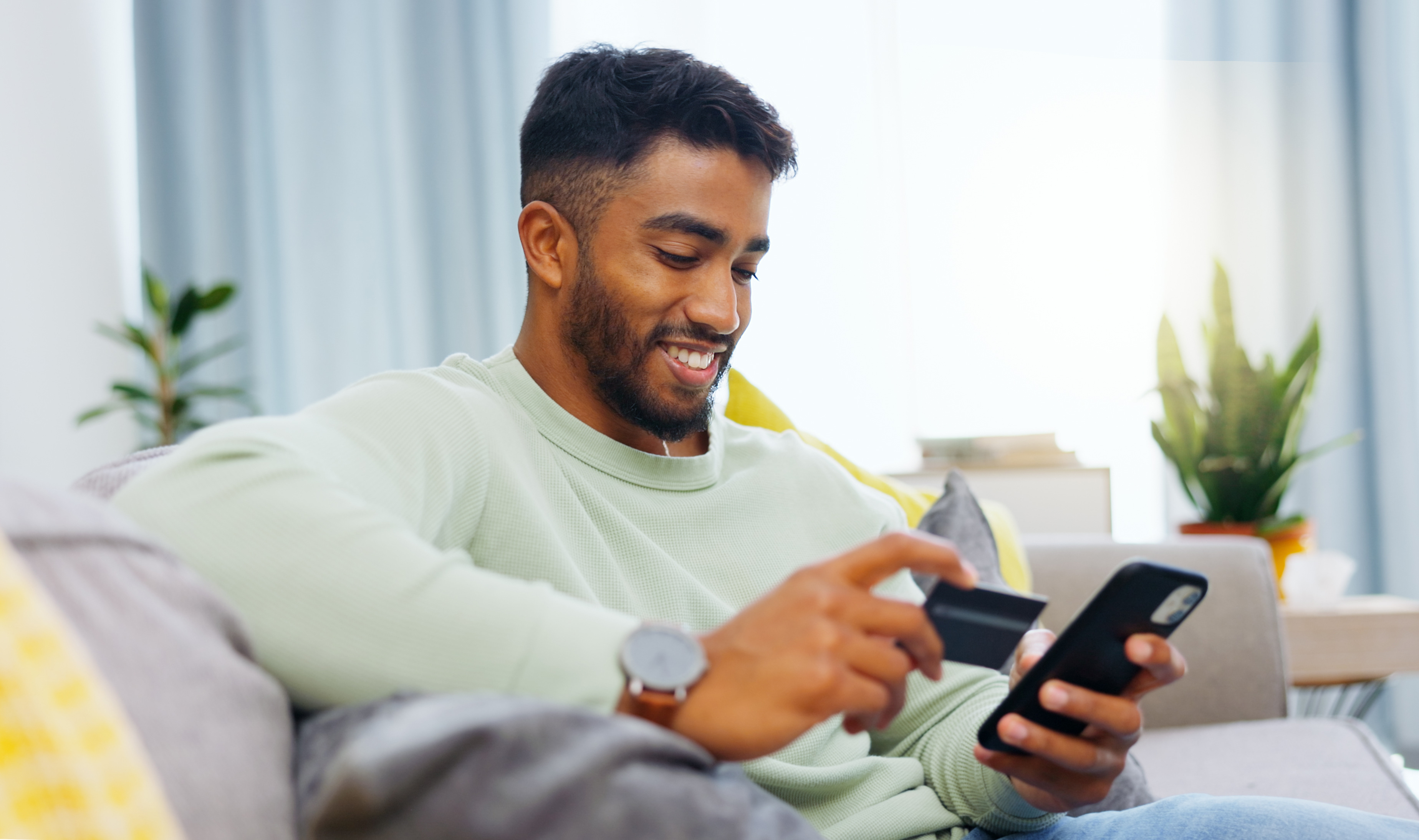 Mann sitzt auf der Couch mit einer Kreditkarte und einem Smartphone